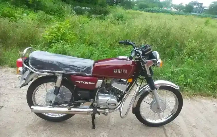 A rider seated on a vintage Yamaha RX100 from 1990, showcasing its iconic silhouette against a serene backdrop.